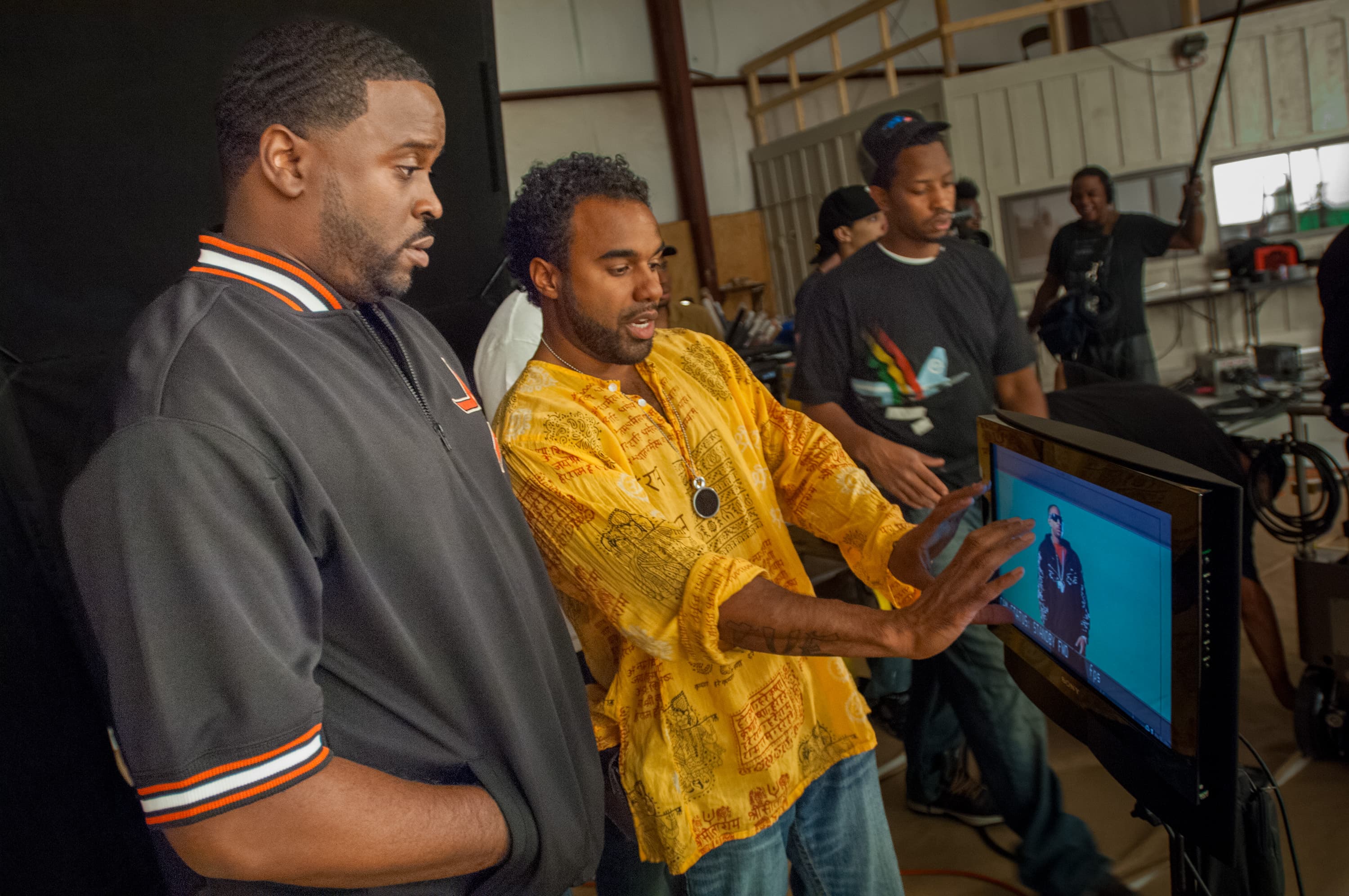 Director Dr. Teeth stands with cinematographer while looking at a video screen showing rapper Ludacris on a green screen while filming a music video