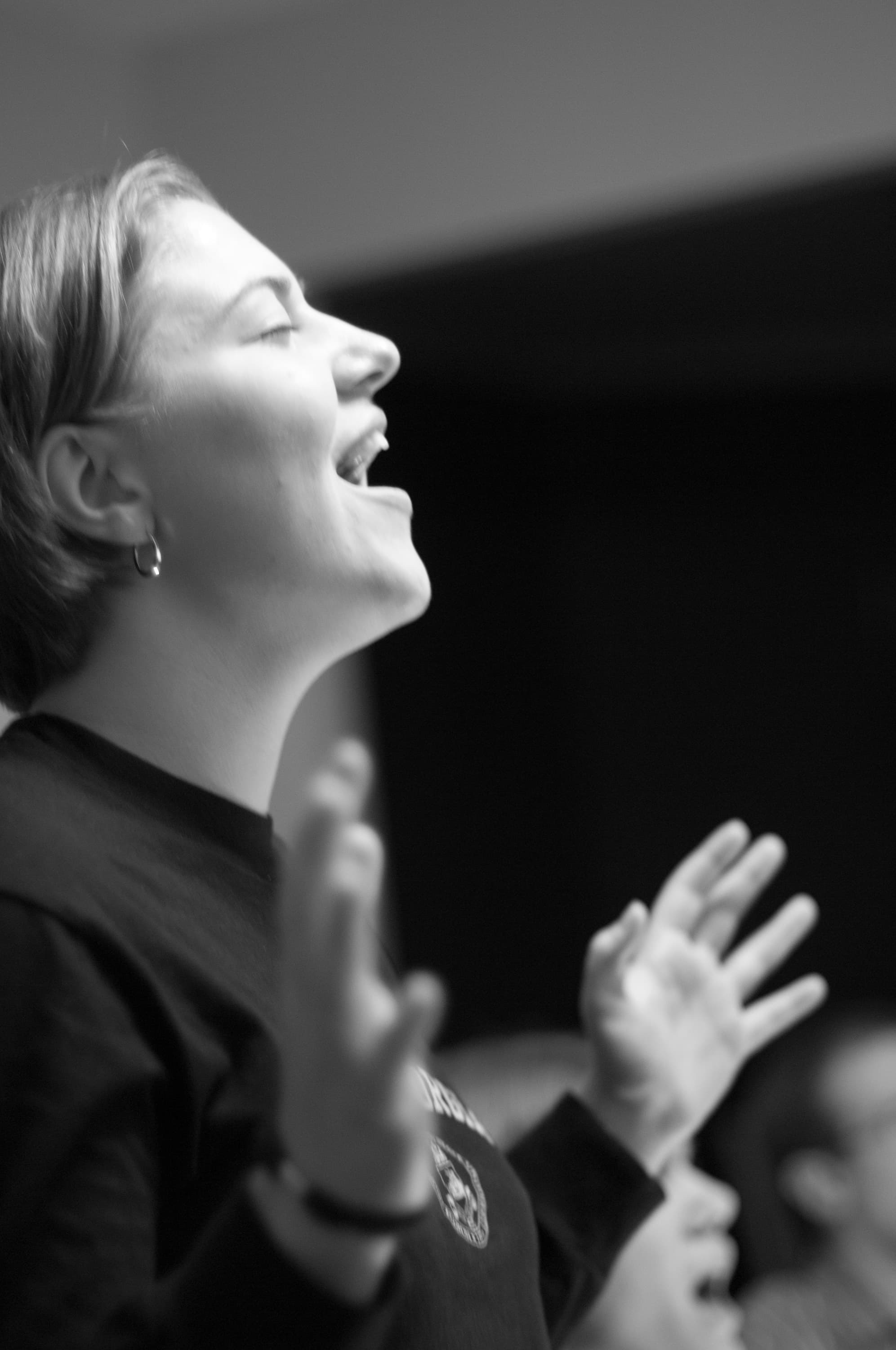 Black and white photo of a person passionately singing or speaking, with eyes closed and hands raised in an expressive gesture, capturing an emotional moment.