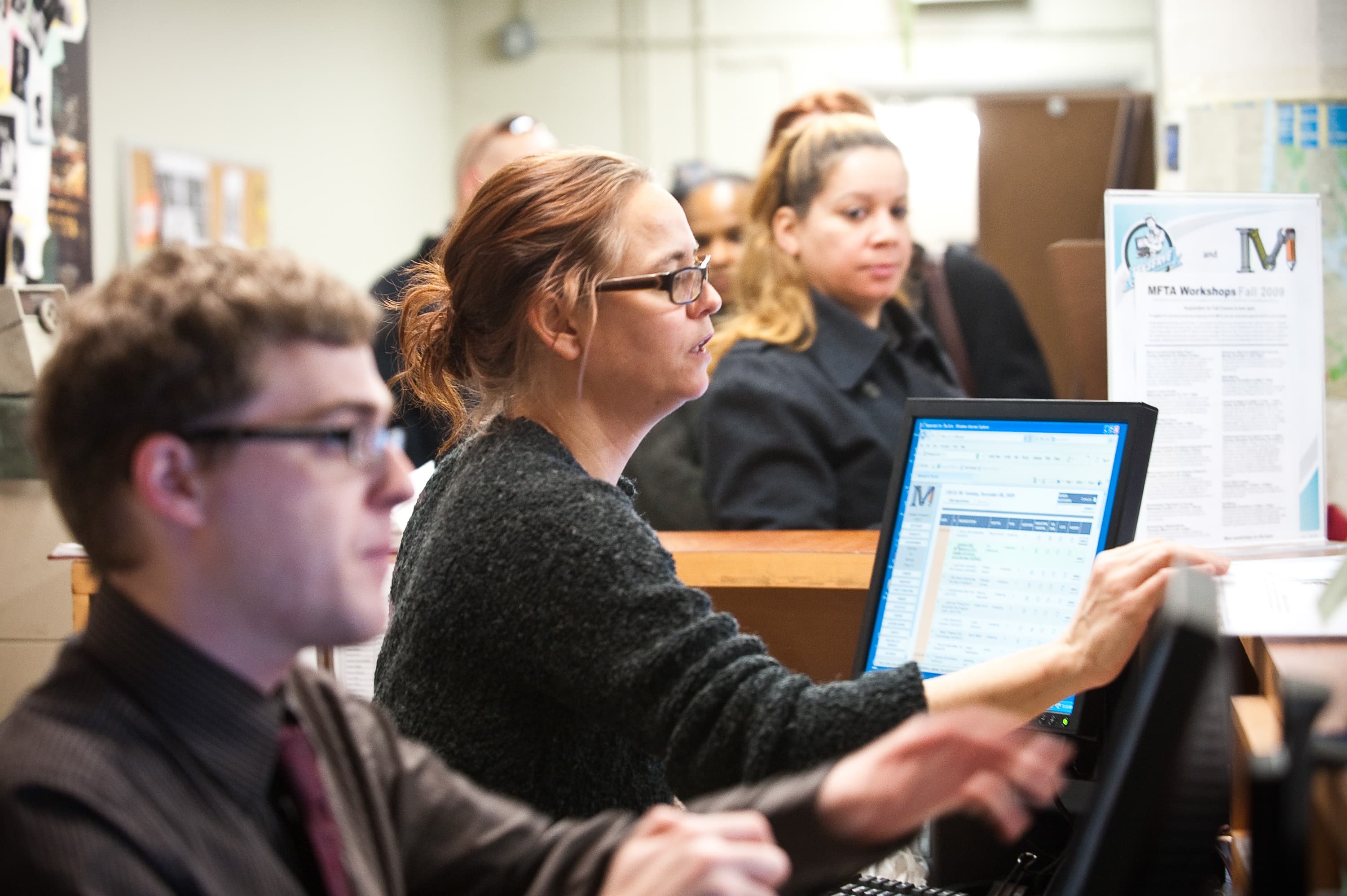 People working at computers in an office with papers on the counter.